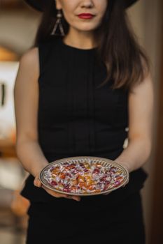 室内，一名黑衣女子拿着一盘色彩缤纷的万圣节糖果