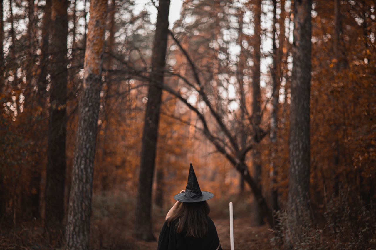 woman in witch costume walking through an autumn forest with vibrant l