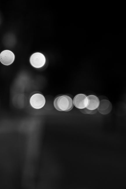 A creative black and white photo capturing bokeh lights against a dark background at night.