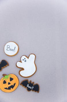 Festive Halloween-themed cookies featuring ghosts, bats, and a pumpkin on a light background.