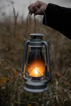 A vintage lantern glowing with warm light, held in a twilight outdoor setting.