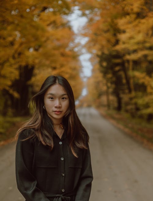 Peaceful young ethnic woman standing on road in autumn woods