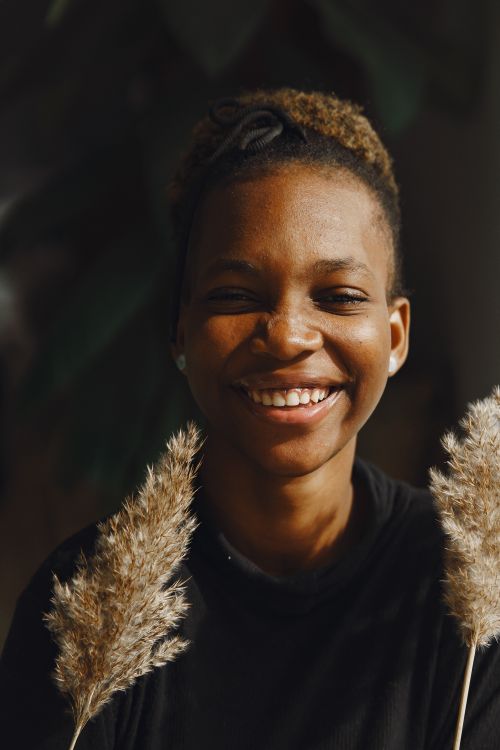 Free Close-up portrait of a smiling young woman holding pampas grass, exuding warmth and happiness. Stock Photo