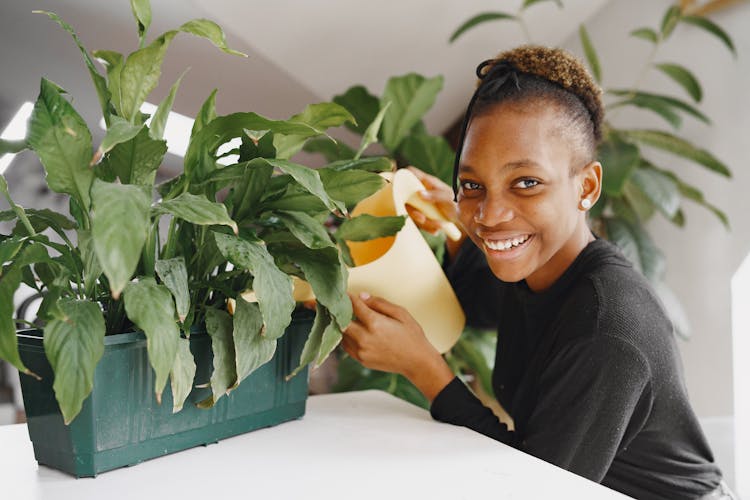 Girl Watering A Potted Plant And Smiling