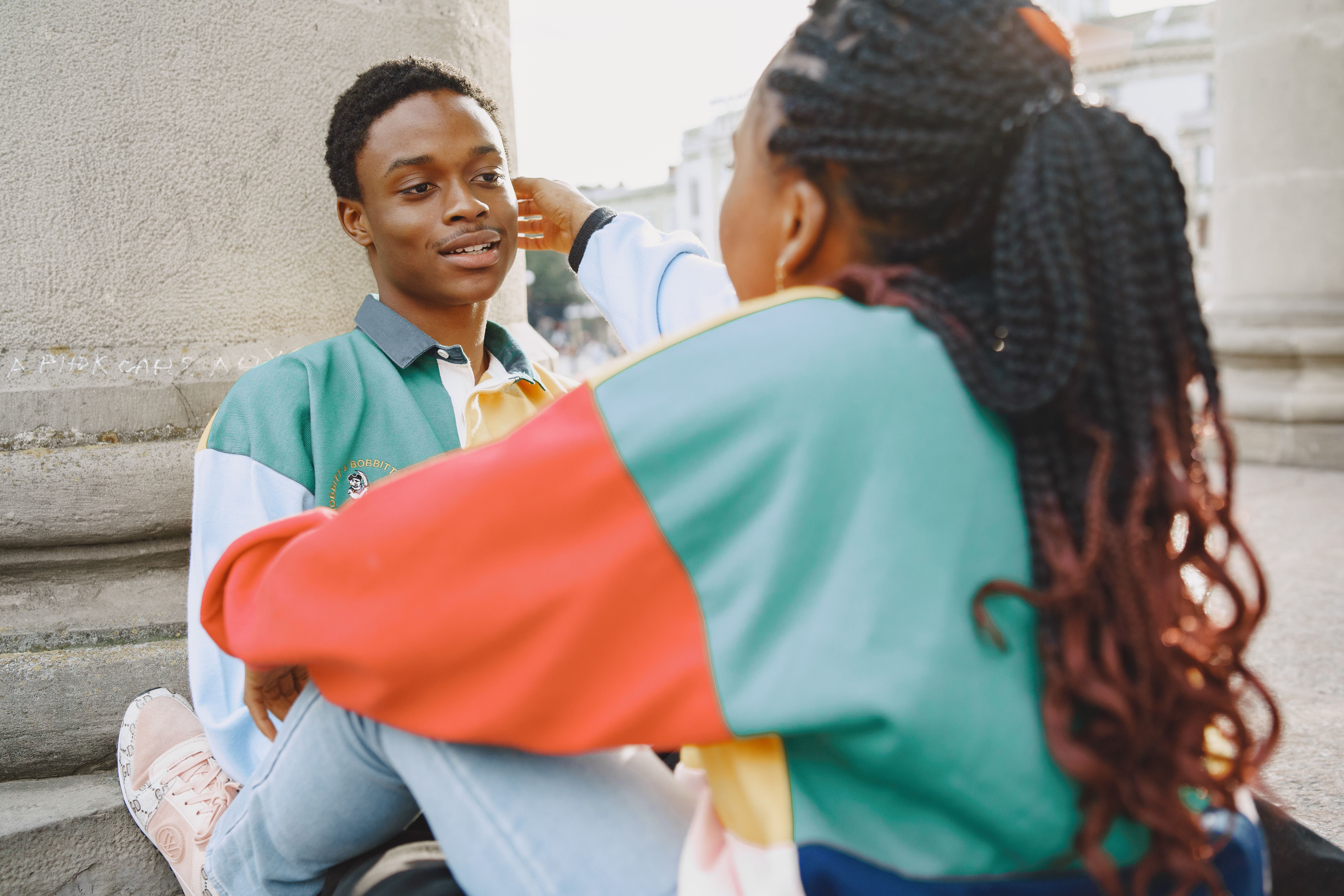 A young couple enjoying a pleasant outdoor moment near city columns, showcasing colorful casual wear.