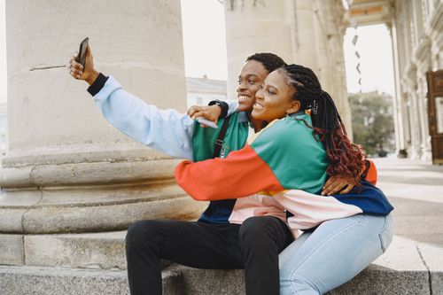 Free Happy couple embracing and taking a selfie outdoors during the day. Stock Photo