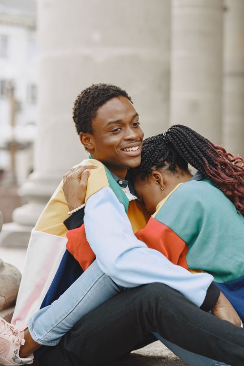 Free A young couple in colorful clothing sharing a warm, intimate embrace sitting outdoors. Stock Photo