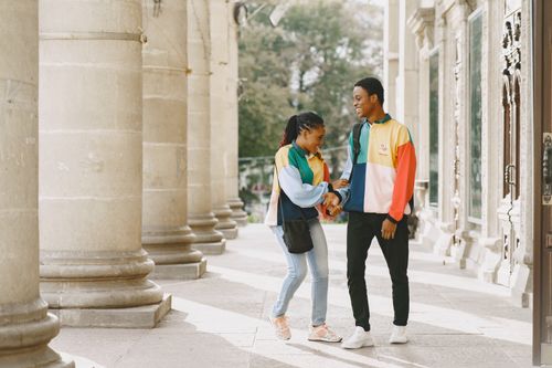 Free Happy couple in colorful jackets enjoying a walk beside historic columns on a sunny day. Stock Photo