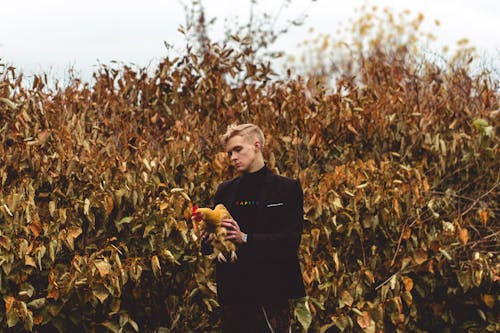 Man Holding a Chicken While Standing near Brown Leaves