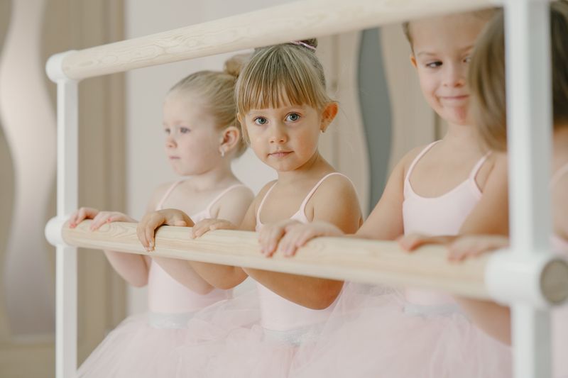 Adorable young girls in ballet class practicing at the barre wearing pink tutus