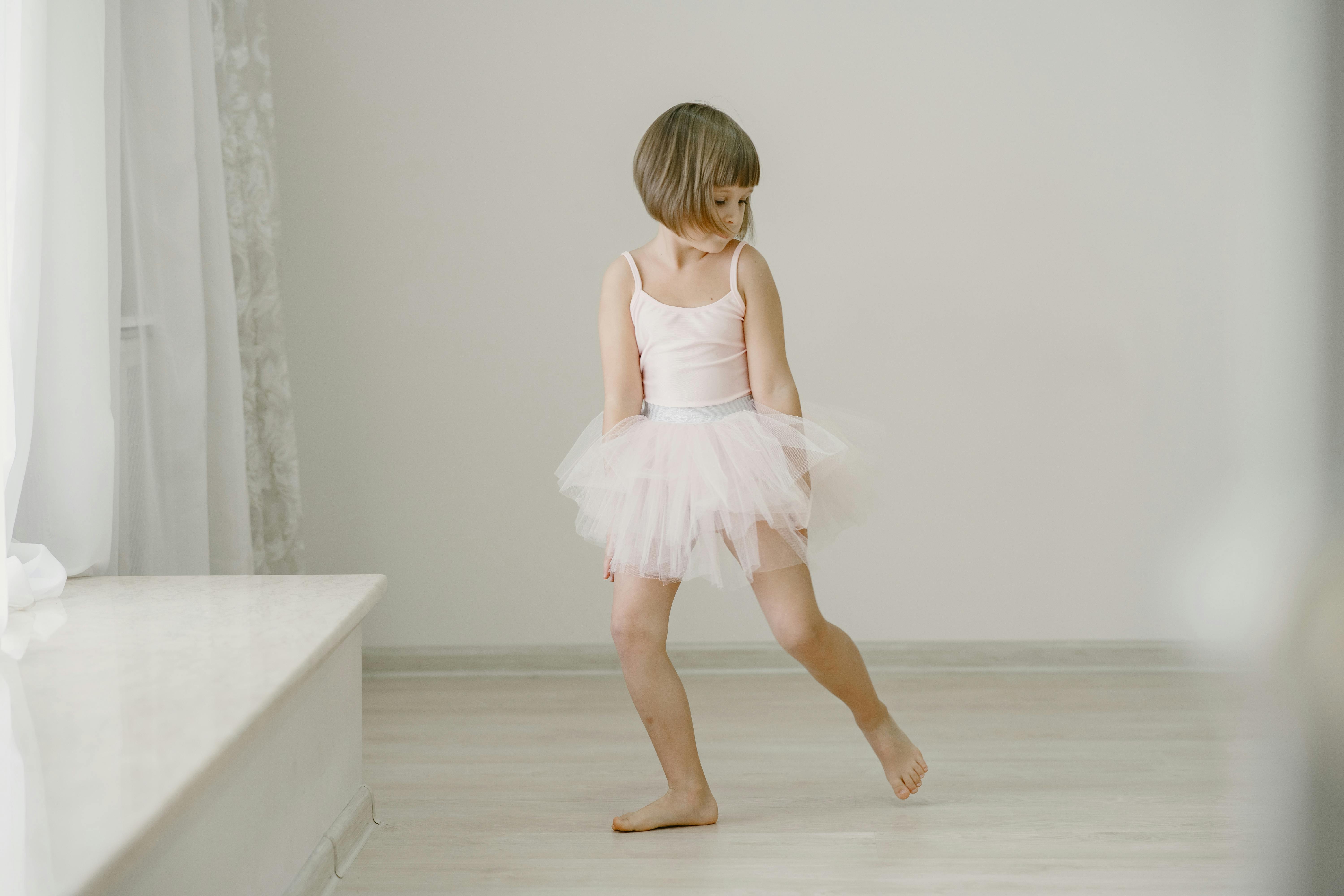 A young girl in a pink tutu practicing ballet inside a brightly lit room.