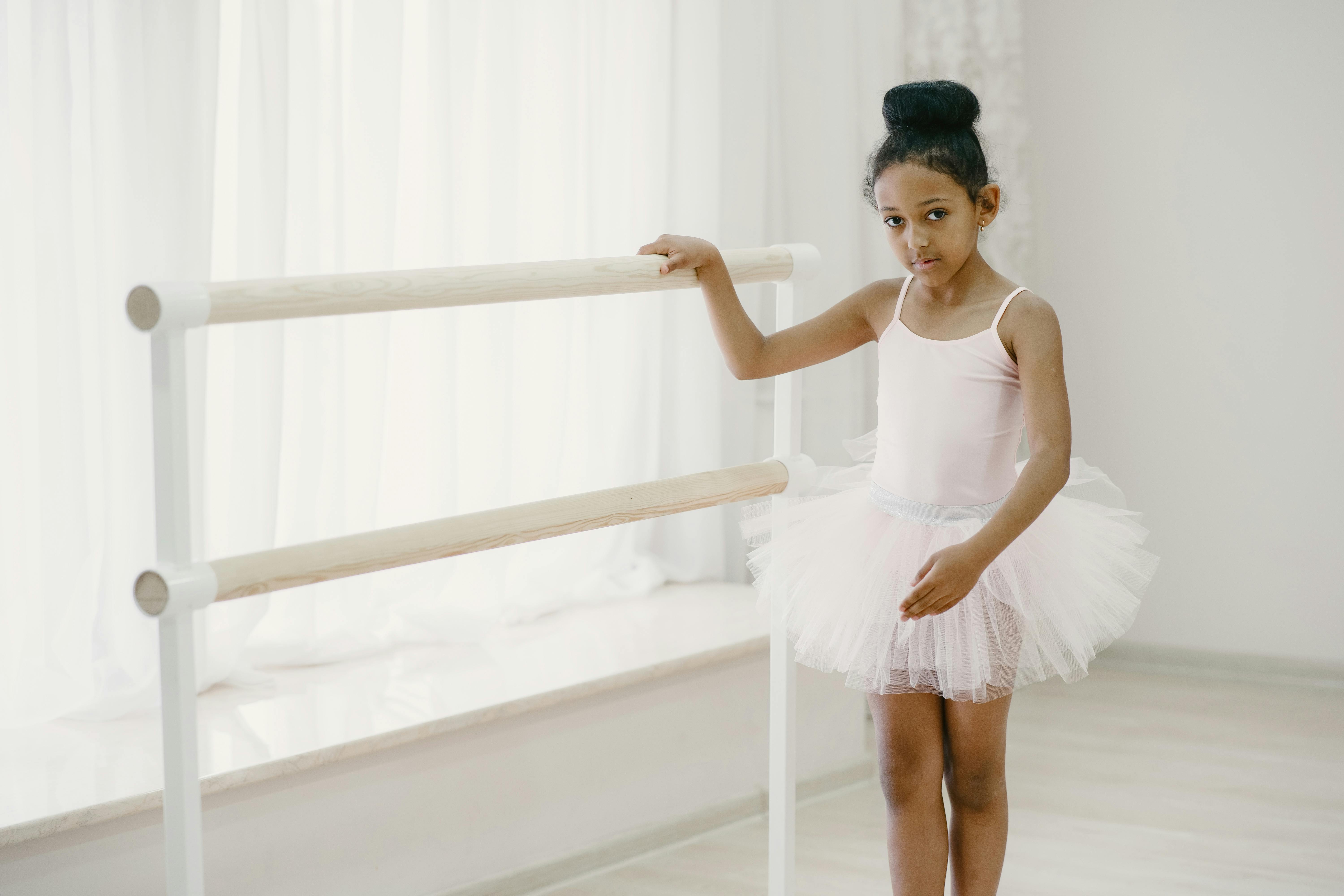 Cute girl in leotard and tights sitting on floor near sofa and putting on  dance shoes before ballet rehearsal at home Stock Photo - Alamy