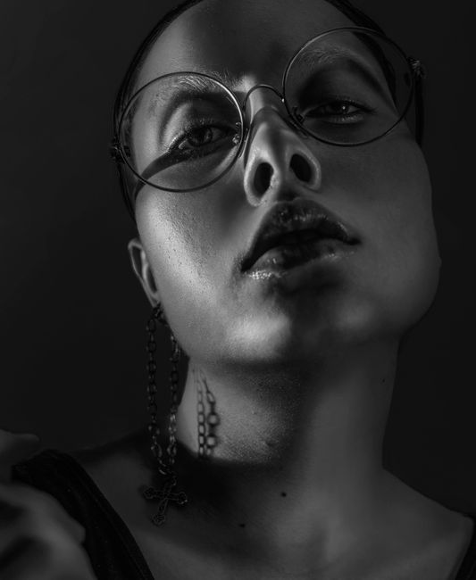 Dramatic black and white close-up portrait of a woman wearing eyeglasses.