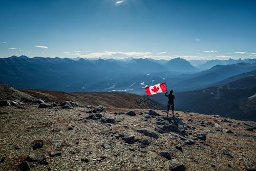 A Person Holding a Canadian Flag on the Mountain Top