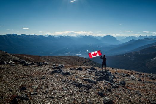 A hiker with a Canadian flag enjoys the stunning mountain views at Jasper, Alberta.