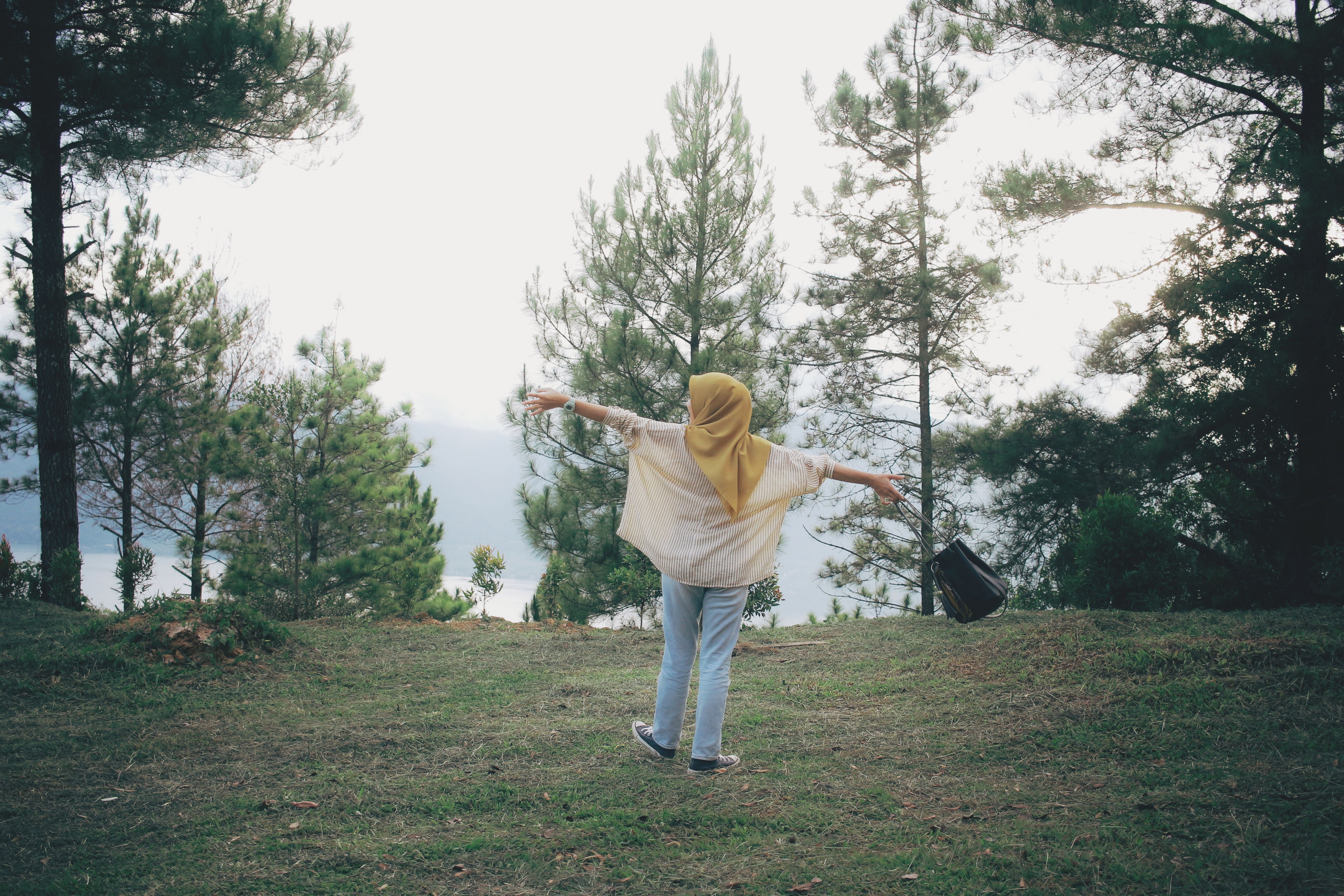 A woman with outstretched arms enjoys nature in a peaceful forest setting, symbolizing freedom and tranquility.