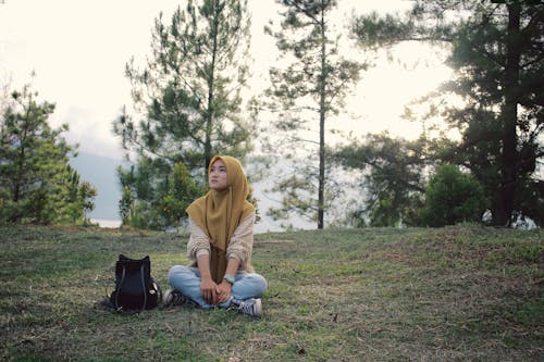Free Woman in Brown Long Sleeve Shirt and Hijab Sitting on the Grass Stock Photo