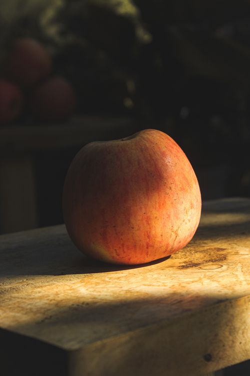 Free A fresh apple placed on a wooden surface with dramatic, shadowed lighting, highlighting its natural texture. Stock Photo