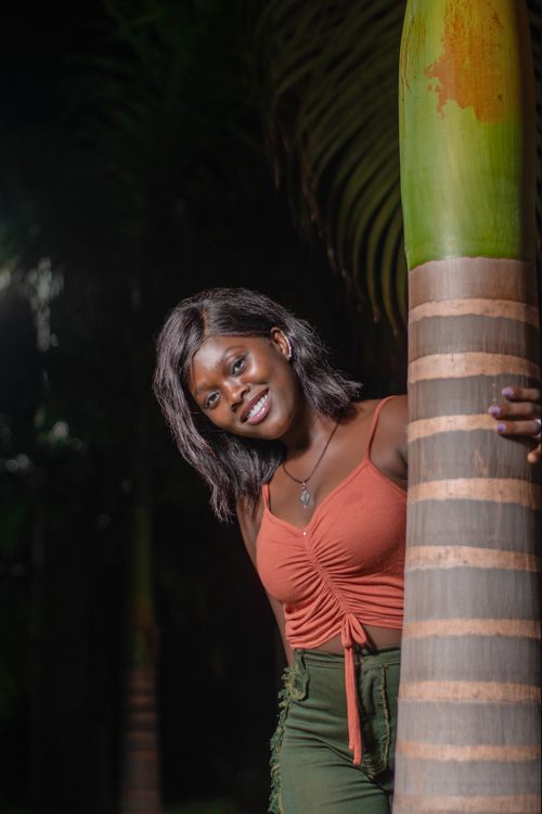Free Elegant woman smiling and posing by a palm tree in a tropical outdoor setting. Stock Photo