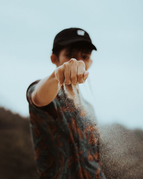 Free Pensive male in casual wear and cap standing with sand in fist falling through fingers Stock Photo