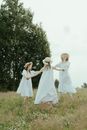 三个女孩穿着白色连衣裙、戴着太阳帽，在阳光明媚的田野里玩耍