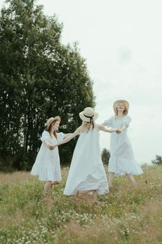 三个女孩穿着白色连衣裙、戴着太阳帽，在阳光明媚的田野里玩耍