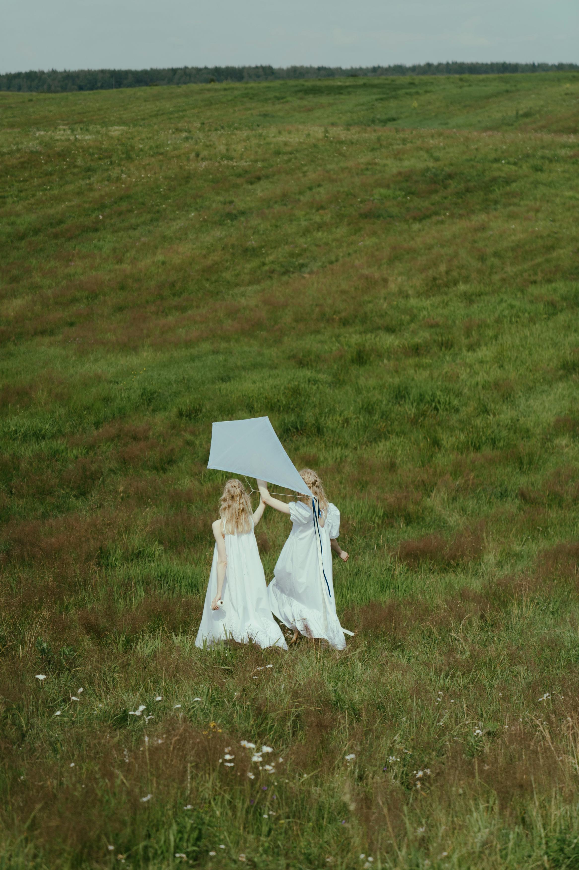 back view of two women walking on grass field while holding a kite