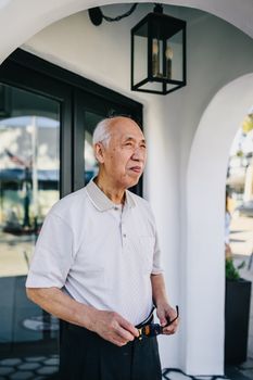 一位资深亚洲男子戴着墨镜，站在时尚拱门下，享受着阳光明媚的一天