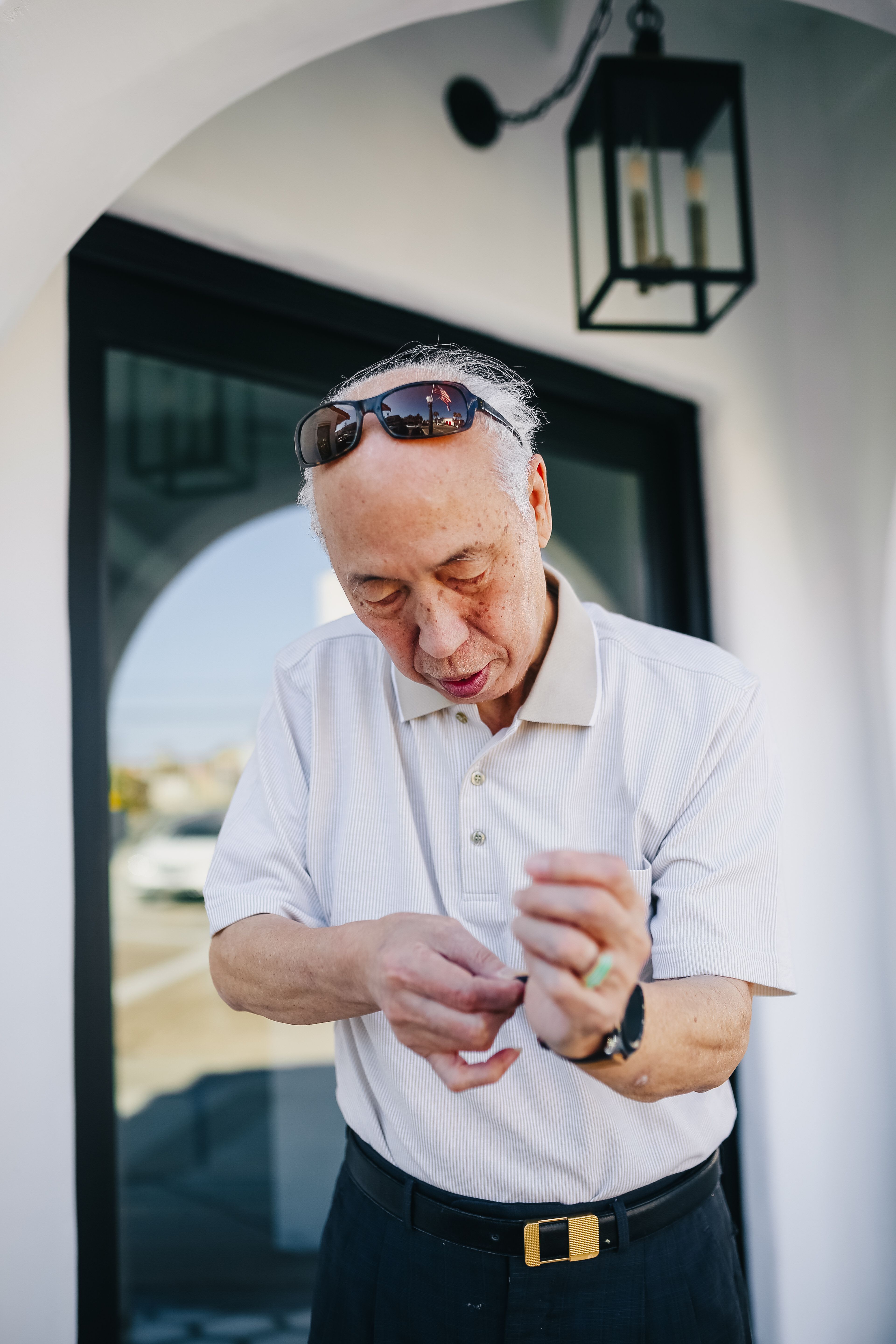 大楼外，一名戴着太阳镜的老人正在调整手表