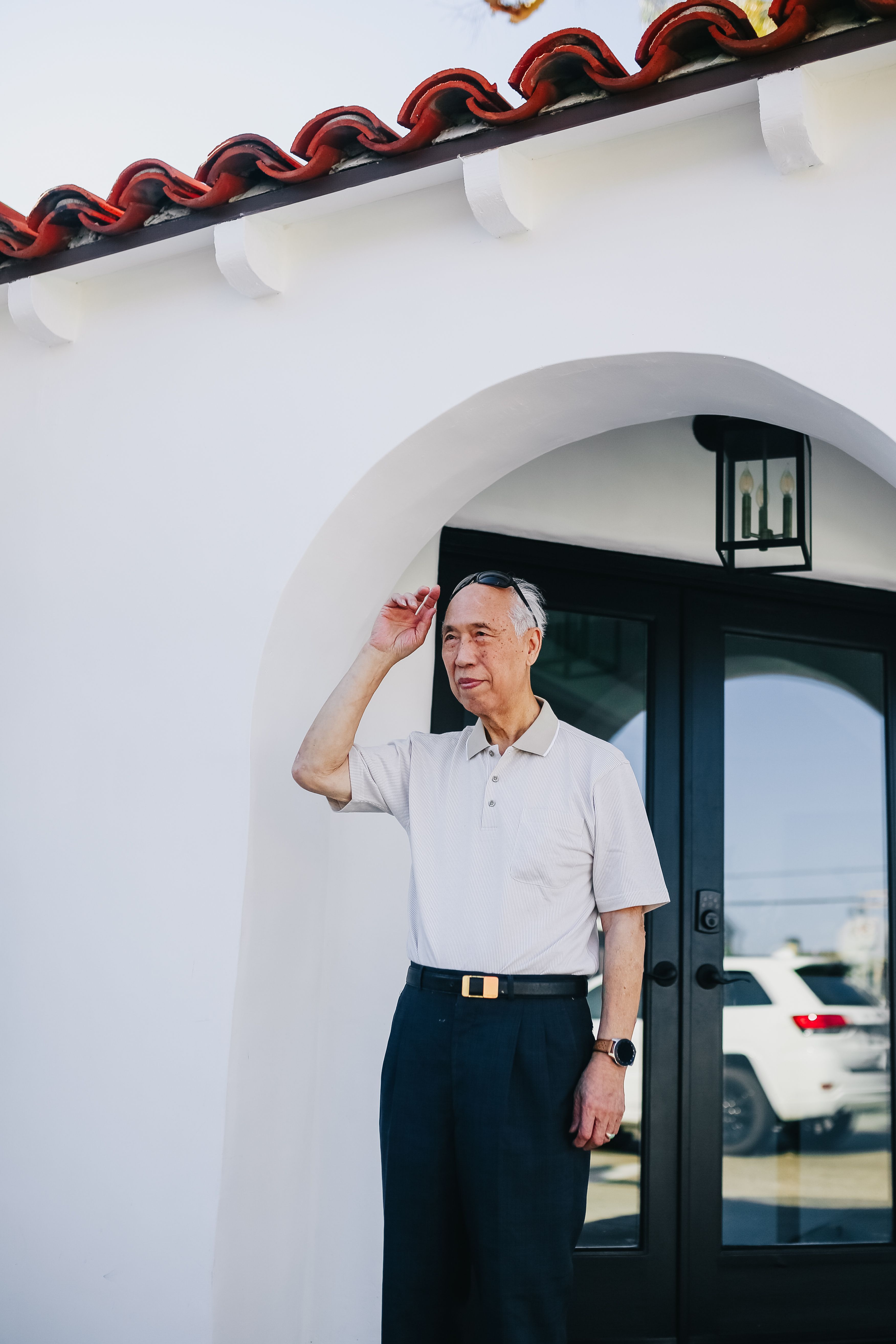 一位穿着休闲装的老人正在现代化的拱形门外等候