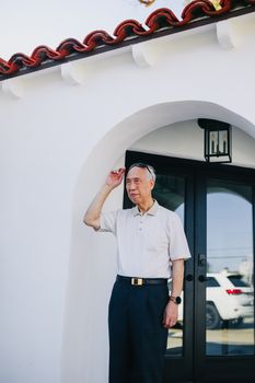 一位穿着休闲装的老人正在现代化的拱形门外等候