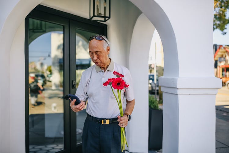 Old Man Holding Red Flowers And Texting On His Smartphone