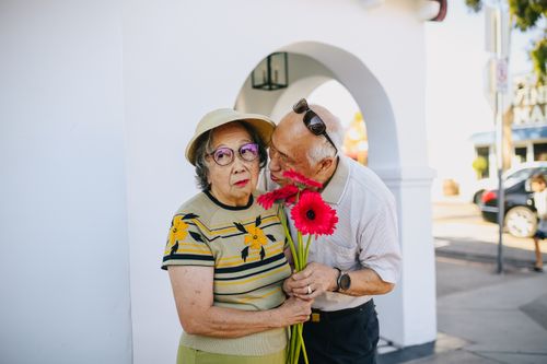Free A senior Asian couple enjoying a tender moment with flowers outdoors, conveying love and affection. Stock Photo