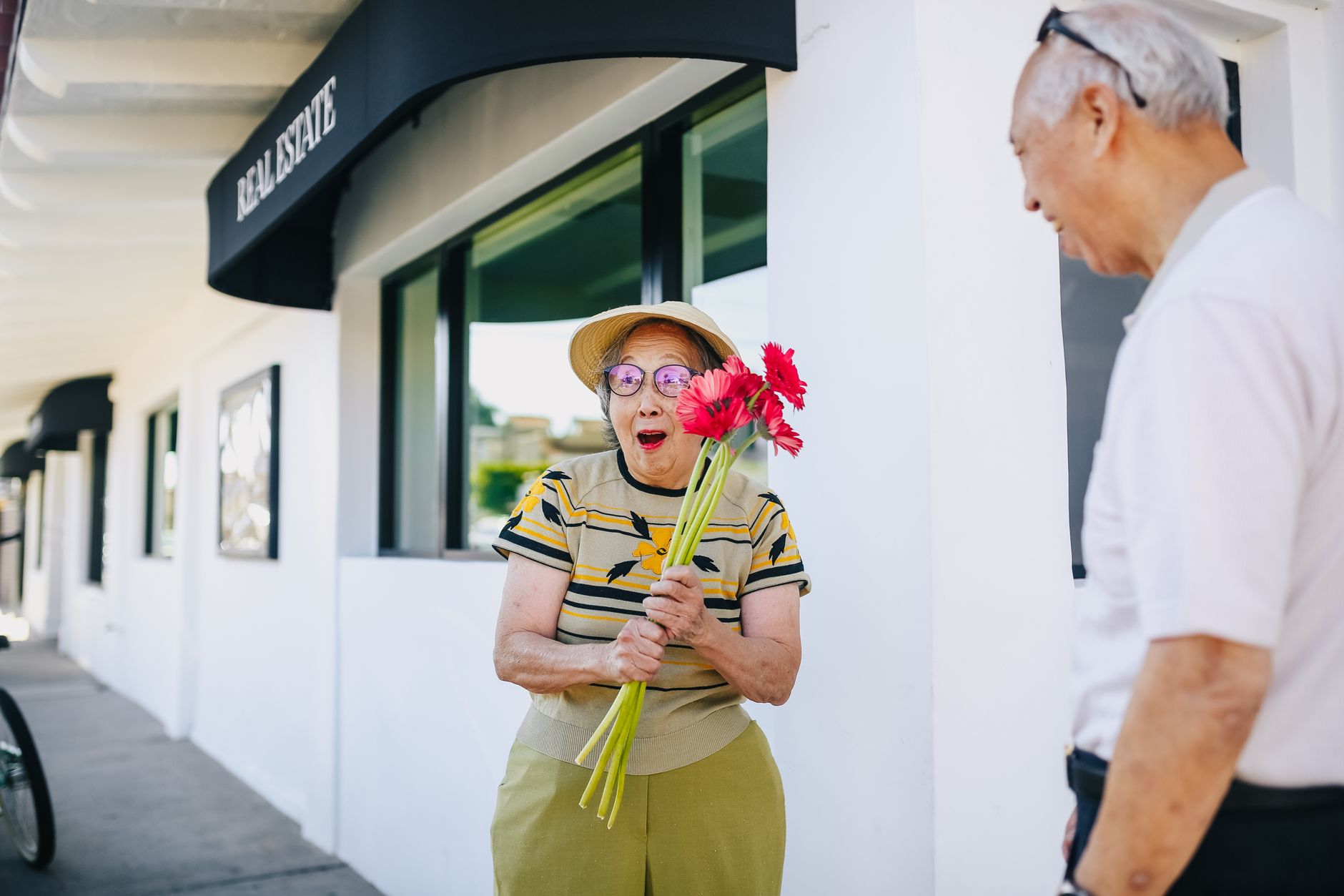 Senior Asian woman surprised with bouquet in lively urban setting, capturing joyful moment.