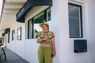 一位面带微笑的老年妇女站在房地产办公室外，享受着阳光明媚的一天