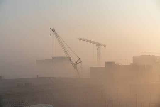 Silhouetted cranes amidst fog at a construction site during dawn in Copenhagen.
