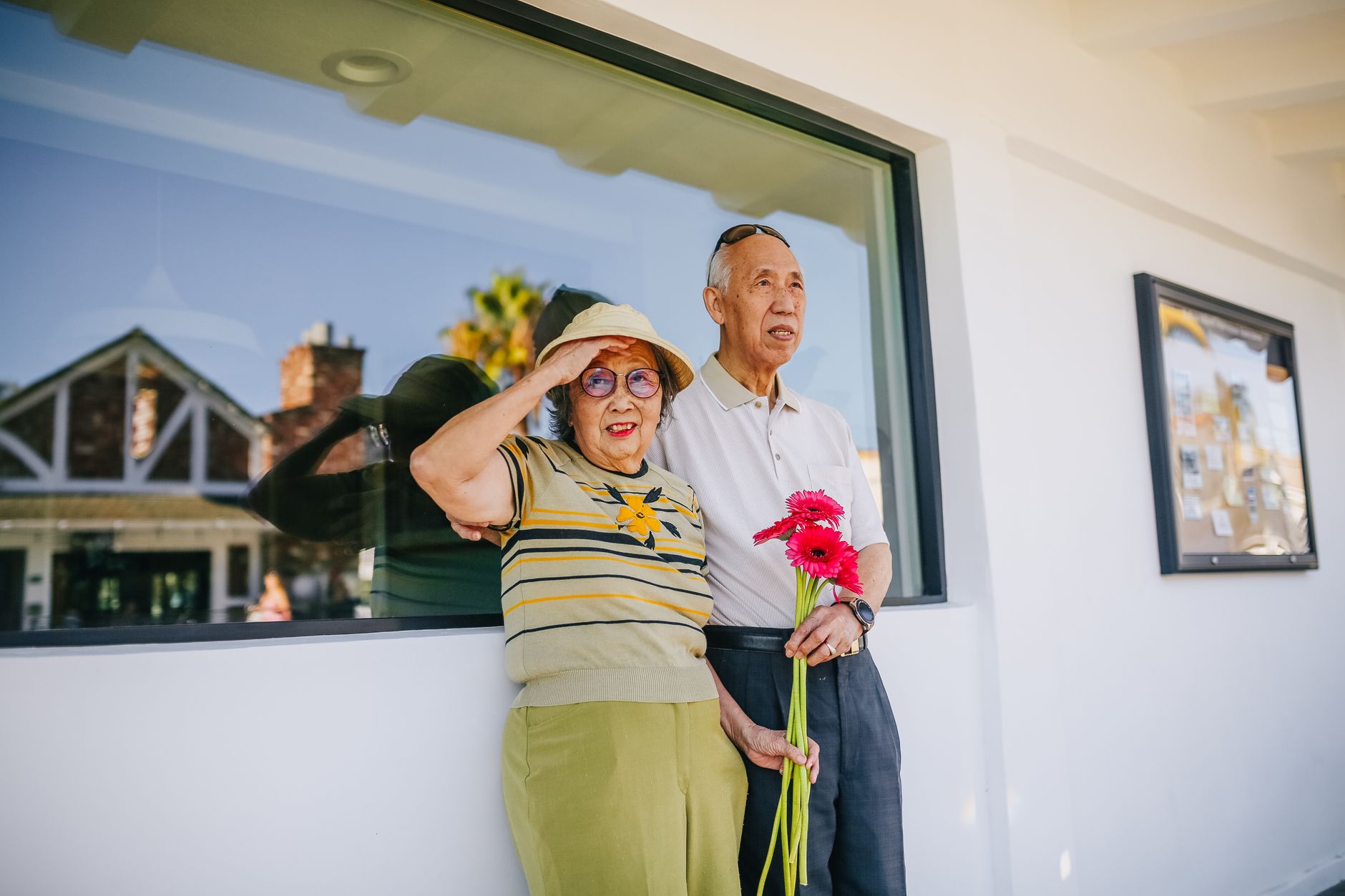 Asian senior couple enjoying a sunny day outside with red flowers, showcasing love and joy.