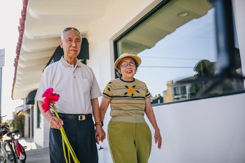 Coppia Di Anziani Che Tengono Le Mani E Che Tengono I Fiori Rossi Mentre Si Cammina