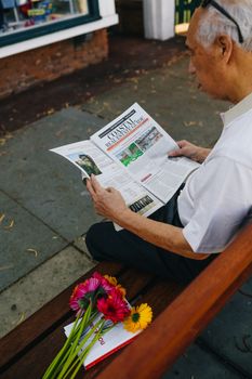 一位老人在公园的长椅上，一边看报纸，一边放着一束五颜六色的鲜花，享受着安静的时光