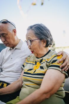 一对亚洲老夫妇坐在户外相拥，享受着宁静的时刻
