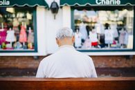 一位白发老人坐在城市街边一家服装店前的长凳上