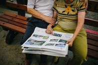 一对老年夫妇坐在公园长凳上，在户外读书、拥抱