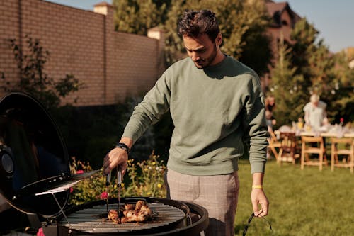 Man in Green Sweater Cooking on Black Charcoal Grill