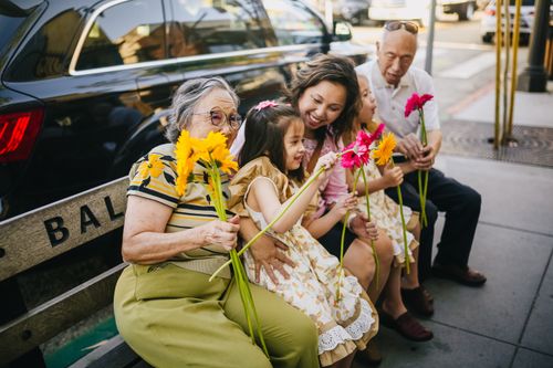 Free Happy multigenerational Asian family sitting together with flowers on a city bench, enjoying a sunny day. Stock Photo