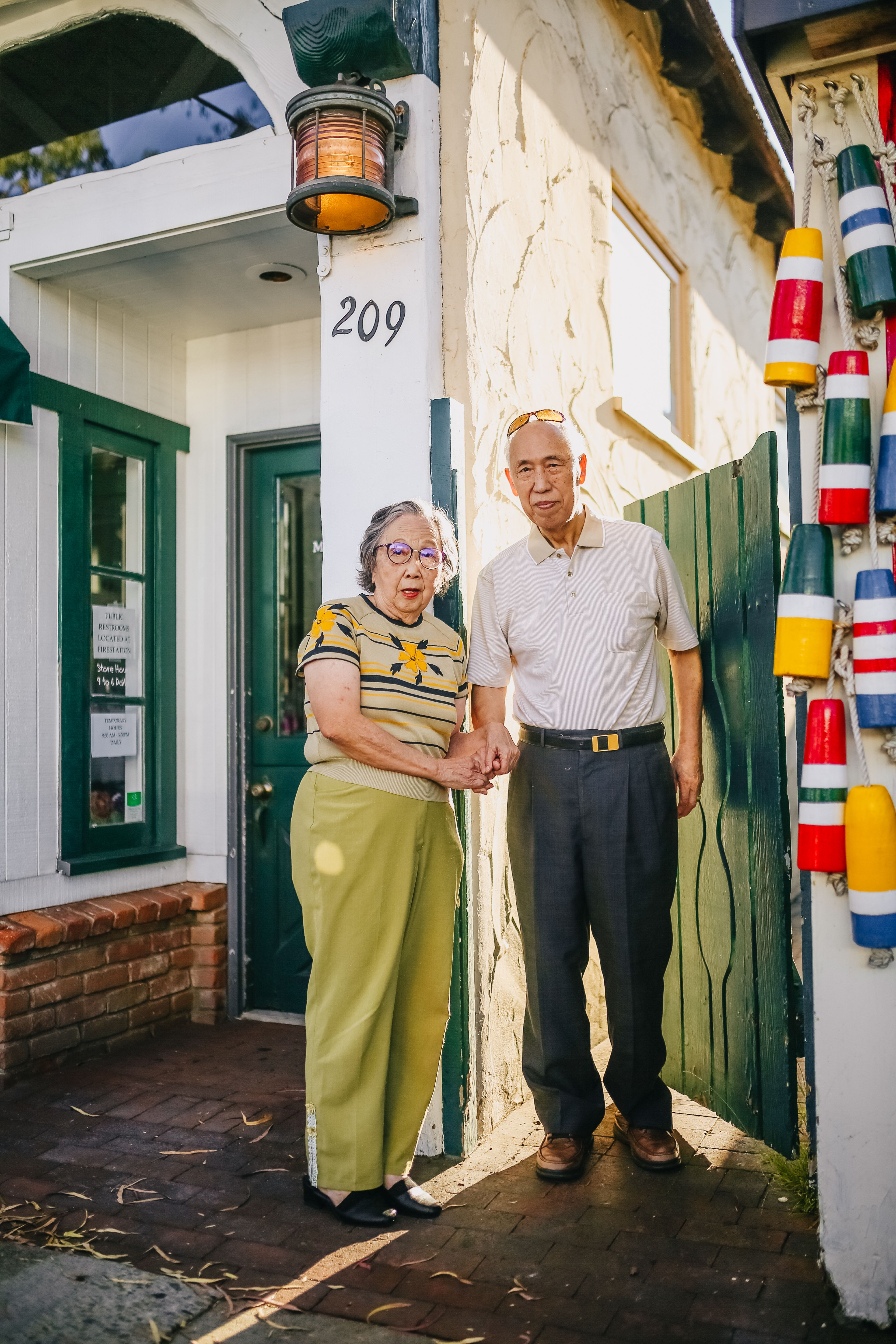 Elderly couple standing happily in front of a charming, colorful house entrance.