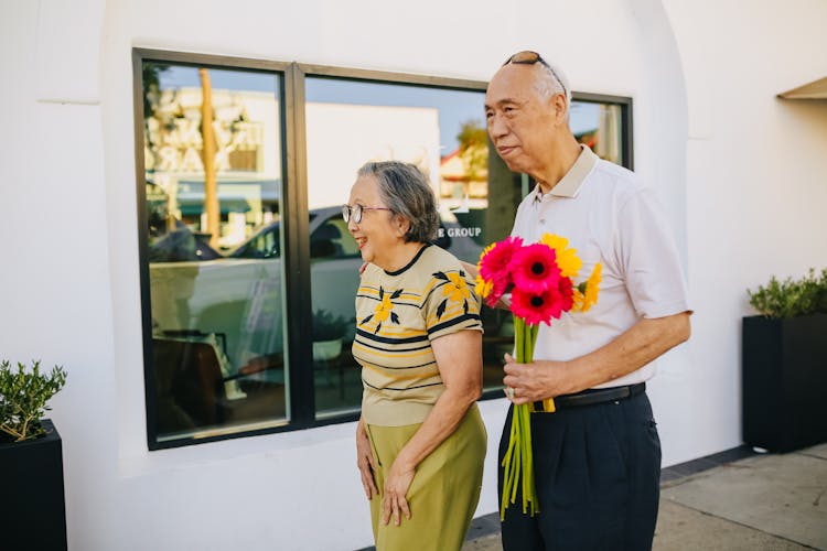 Elderly Man Holding Flowers While Walking With His Wife