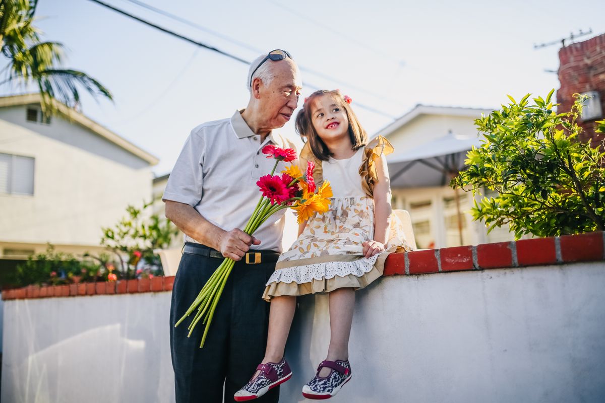 Asian grandfather holding flowers with his young grandchild outdoors