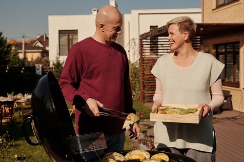 Free Smiling couple grilling vegetables outdoors in backyard during a sunny day. Stock Photo