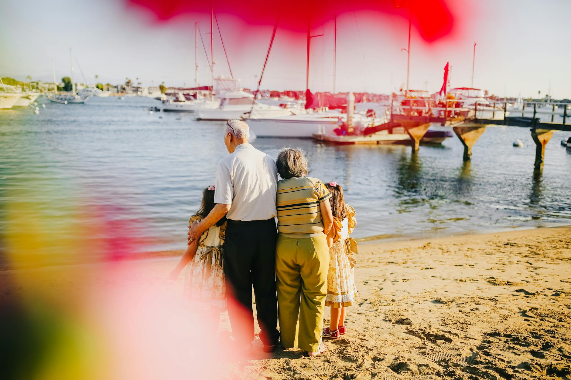 Elderly couple with grandchildren enjoying a sunny day on the beach, overlooking the sea with boats.
