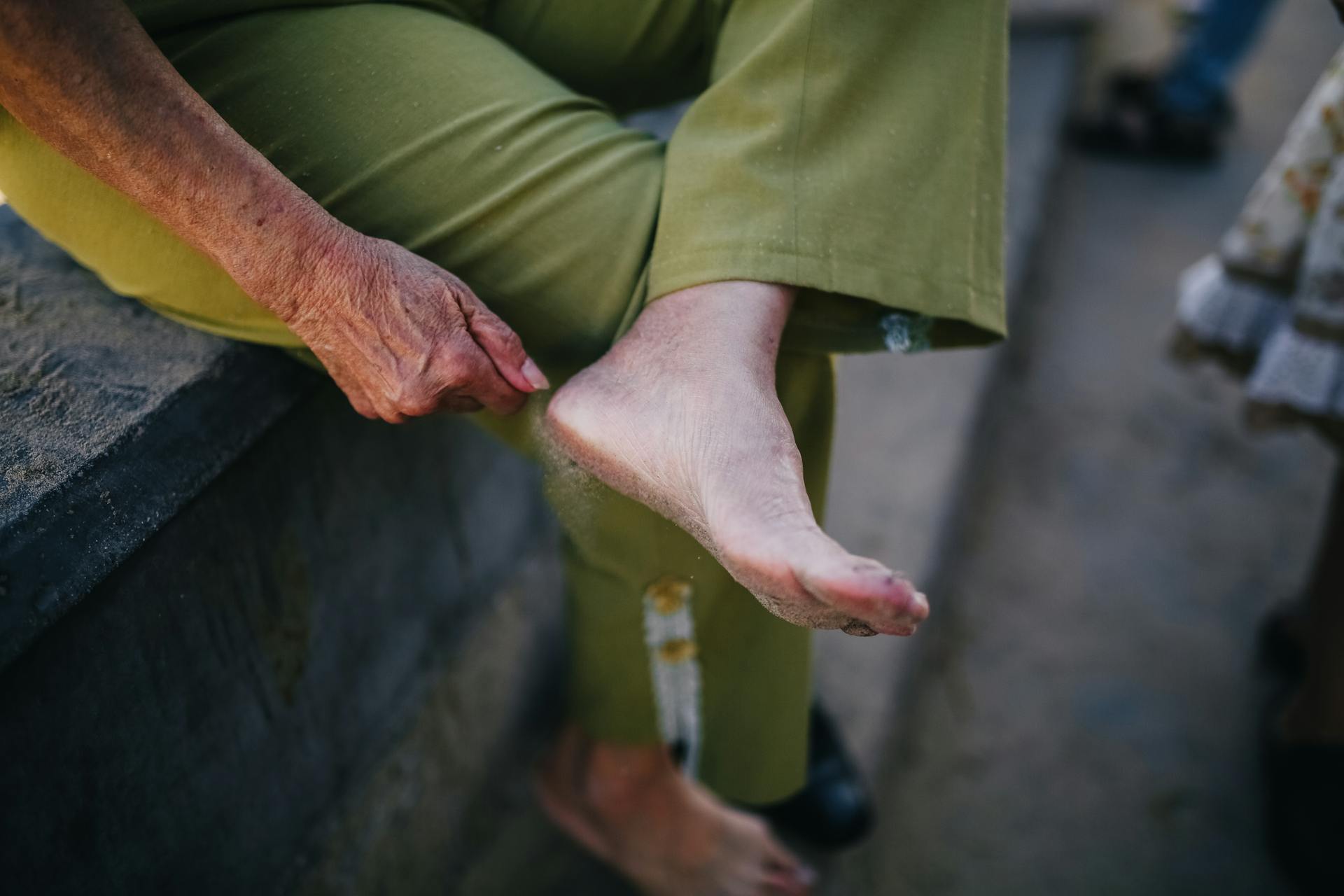 A senior person sitting on a bench outdoors, resting one foot comfortably.